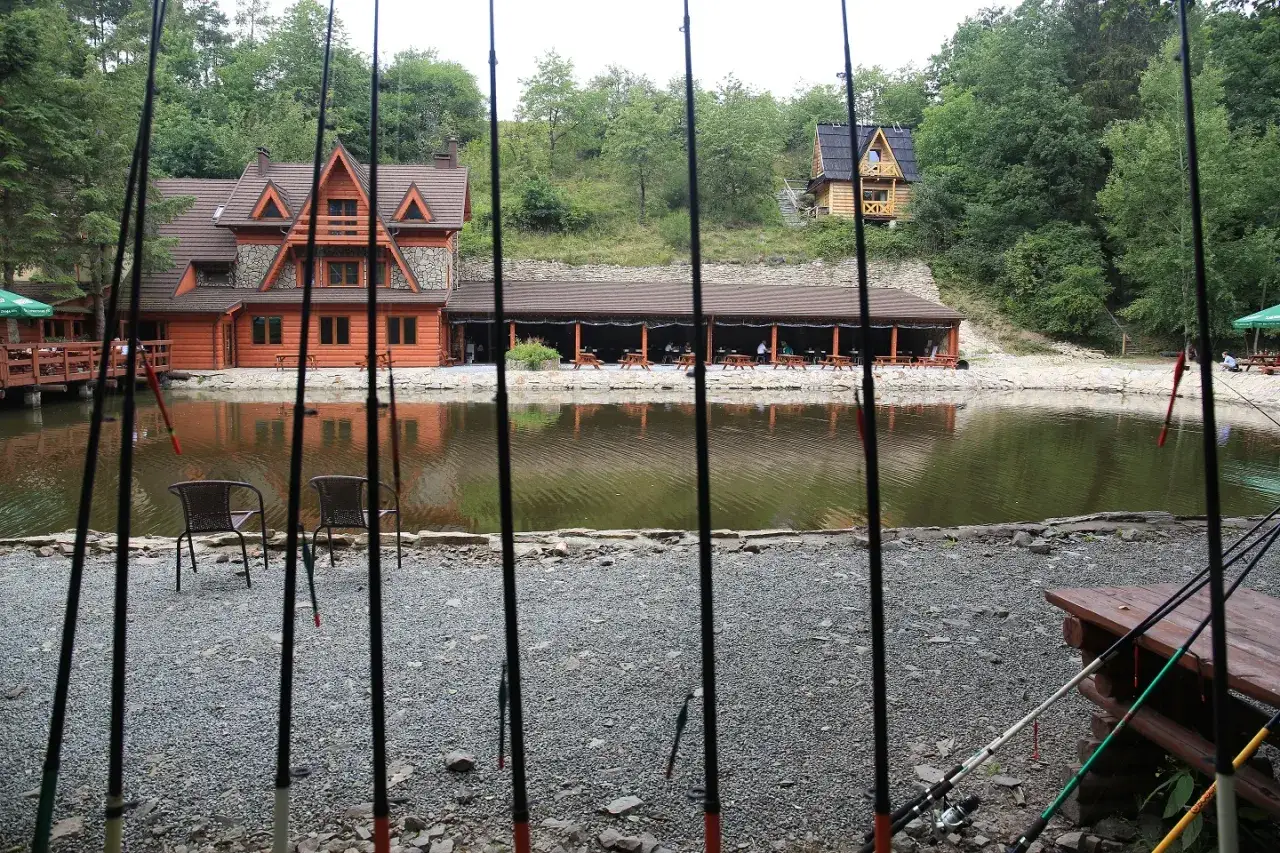 Smażalnia i łowisko pstrągów pod dębem. Wędki czekają nad wodą, a drewniane domki zapraszają na posiłek.