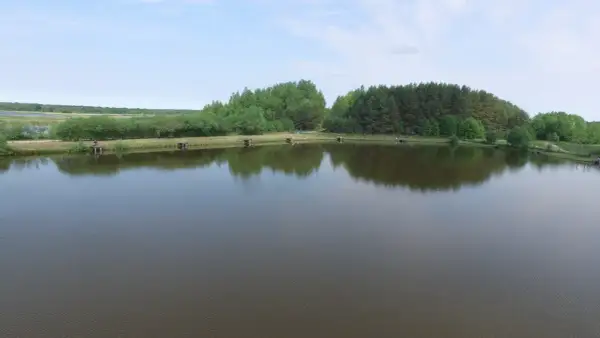 Widok na łowisko z pomostami i drzewami w tle, odbijającymi się w spokojnej wodzie.