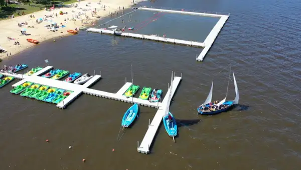 Na plaży i w wodzie widać ludzi, łódki, rowery wodne i pływający basen. To idealne miejsce na wypoczynek, jak kokotek łowisko Leśnica.