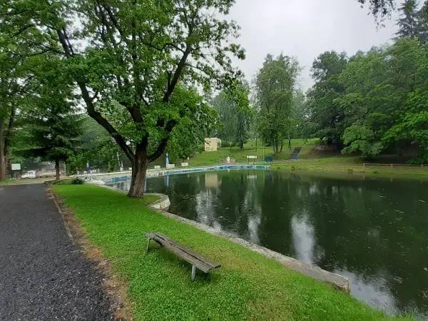 Spokojne stawy w Lądku-Zdroju, otoczone zielenią, zapraszają do odpoczynku. W oddali widać basen.