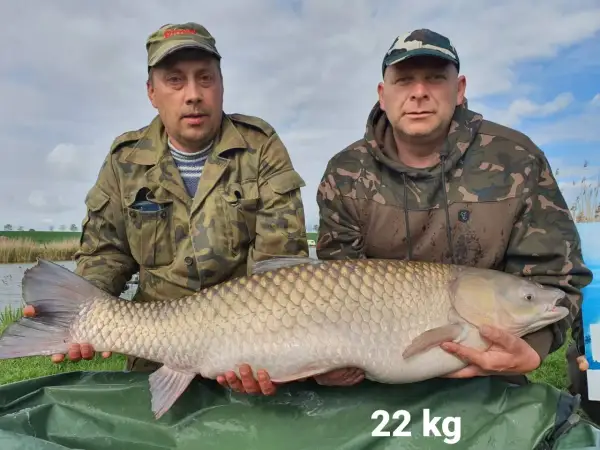 Dwóch wędkarzy prezentuje imponującego karpia o wadze 22 kg, złowionego na łowisku Nowe Żukowo.