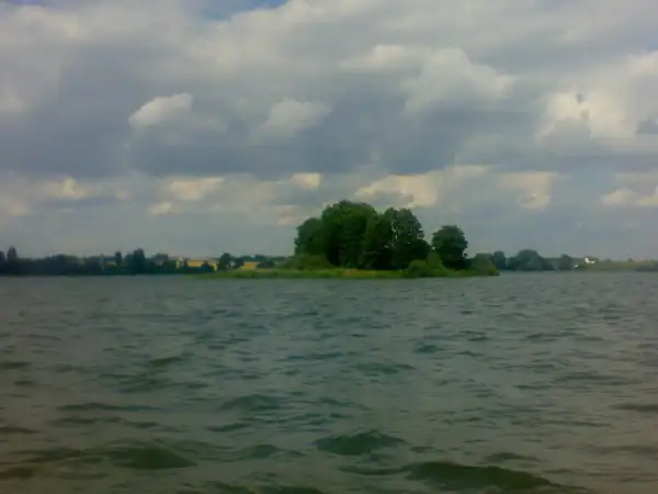 Spokojne jezioro Głuszyńskie, idealne na wędkowanie. Na horyzoncie zielone drzewa i chmury.