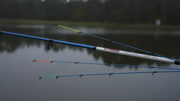 Wędki Robinson Stinger Method Feeder z kolorowymi szczytówkami na tle spokojnej wody i drzew.