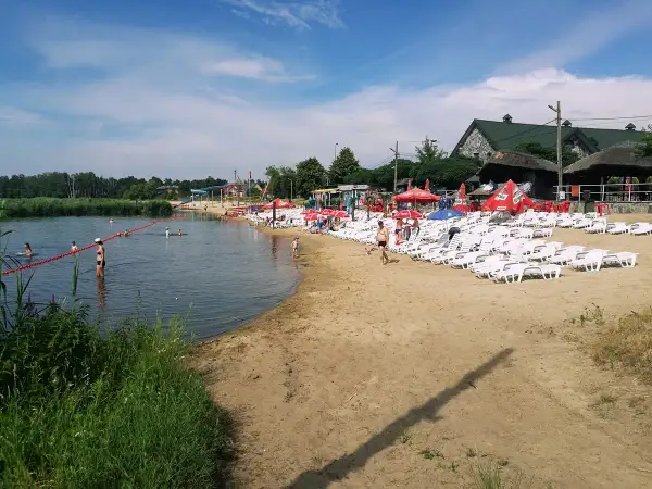 Słoneczny dzień na plaży, gdzie łowisko wilga wodna kraina zaprasza do kąpieli i relaksu. Leżaki i parasole czekają na plażowiczów.
