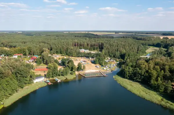 Widok z lotu ptaka na jezioro, plażę z ludźmi, kemping i las. Sprawdź jezioro przechlewskie cennik na wakacje.