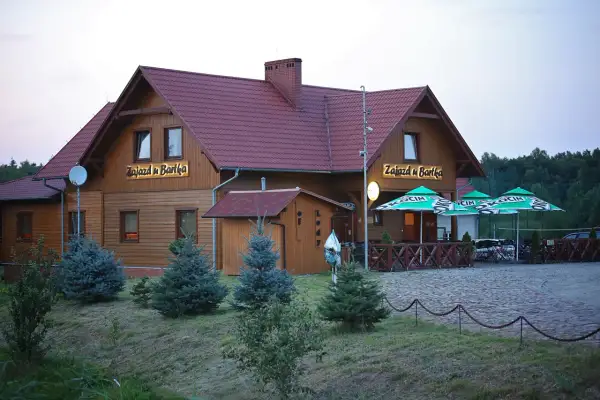 Drewniany budynek z napisem "Zajazd u Bartka" i zielonymi parasolami przed wejściem.